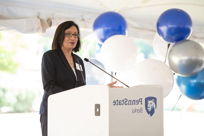 Penn State President Neeli Bendapudi speaks at a podium displaying the Penn State Berks mark, with blue and white balloons in the background. 