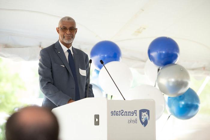 Penn State Berks Chancellor George Grant Jr. standing a podium with the Penn State Berks mark and blue and white balloons in the background.