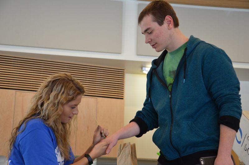 A student painting a green dot on another student's hand