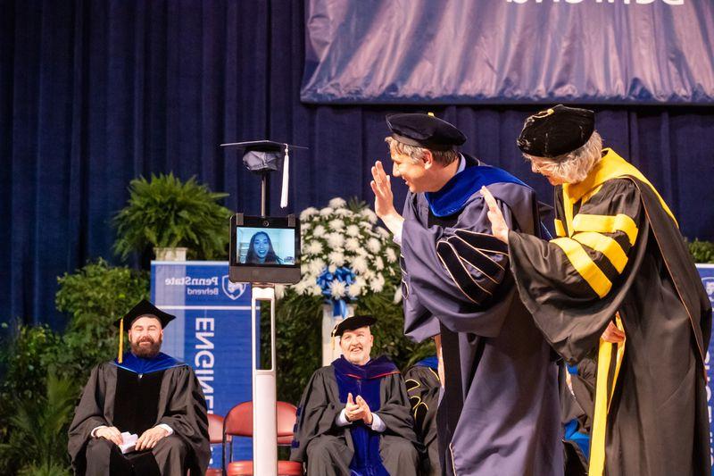 Two Penn State Behrend faculty members wave to a student whose face is on the monitor of a robot.