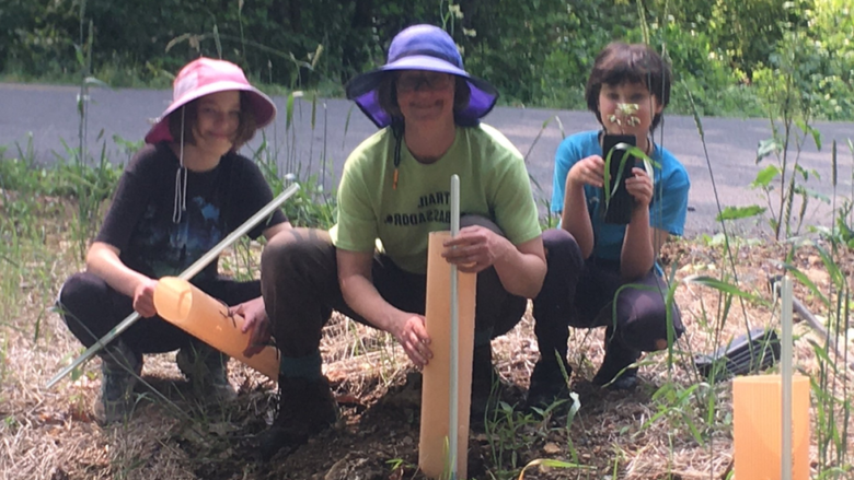 Jayne crouches on the ground with two kids as they do yard work