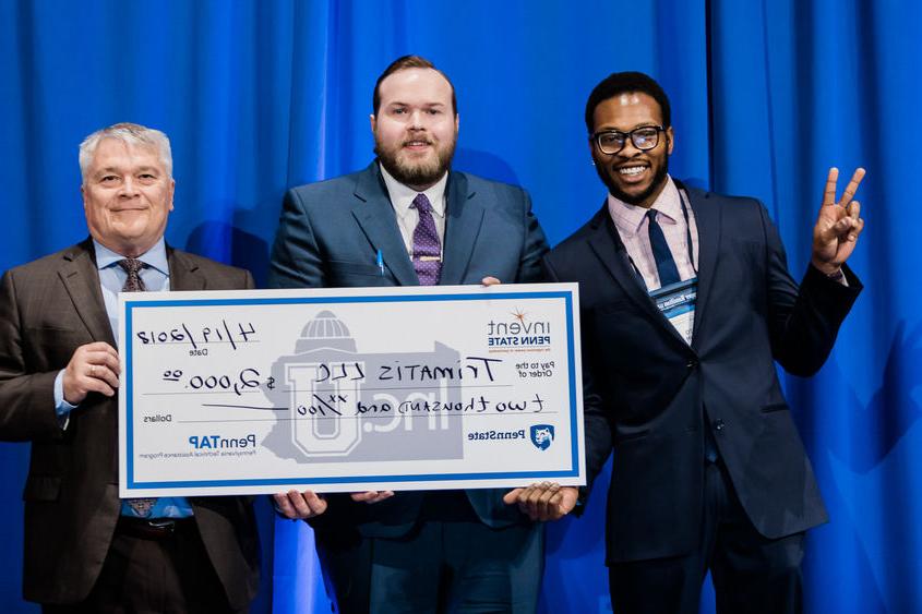 Penn State President Eric Barron, right, awards $2,000 at the 2018 Invent Penn State Venture & IP Conference to Trimatis' Tito Orjih, left, and Jason Lehrer.