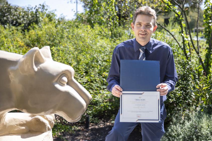Brett Spencer holding award next to Nittany Lion statue