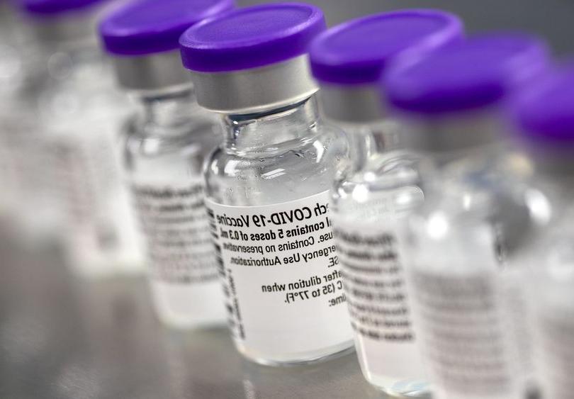 A row of vials show labels indicating they contain the COVID-19 vaccine.