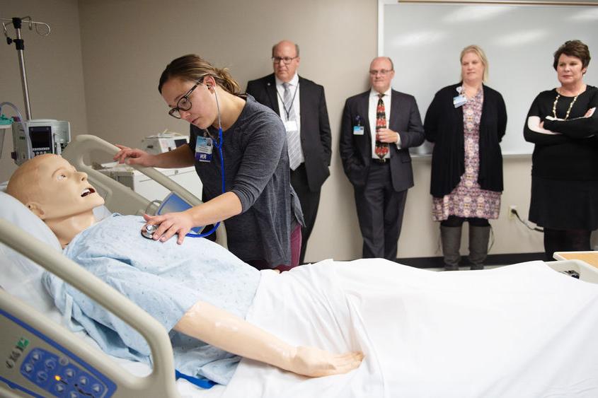 A nurse leans over a mannequin to demonstrate a medical technique