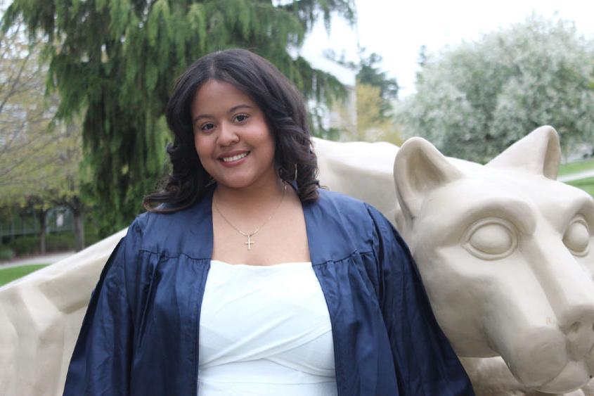 Aidee Santos Acosta poses in front of Nittany Lion Statue in grad gown