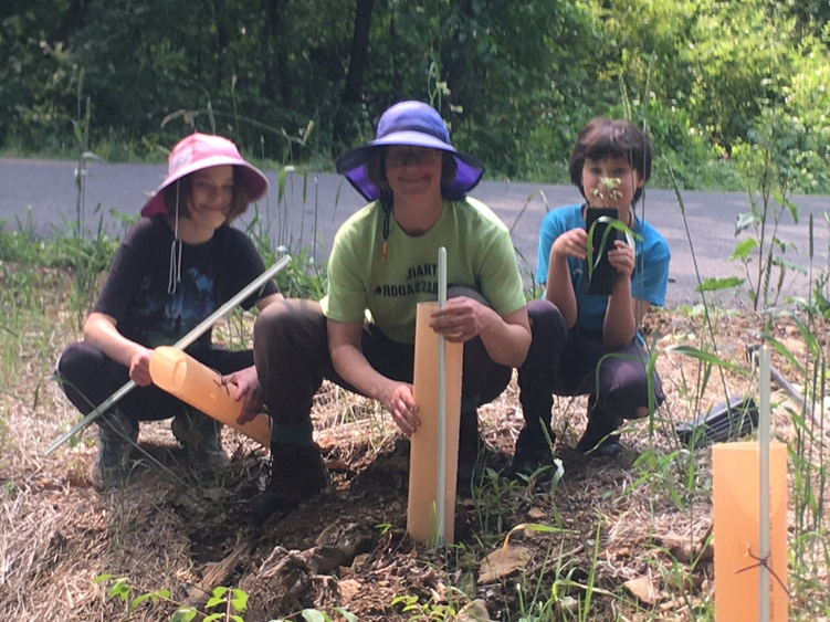 Jayne crouches on the ground with two kids as they do yard work