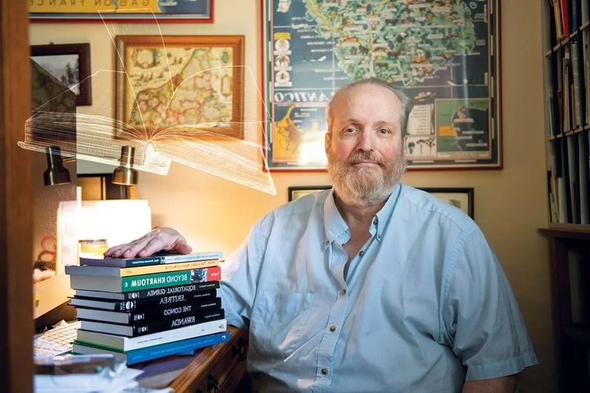 Randall Fegley sits at desk with books on top of it