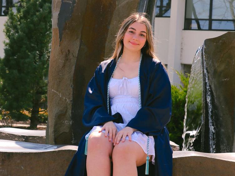 Sam Hagenbush wearing graduation cap sitting in front of fountain